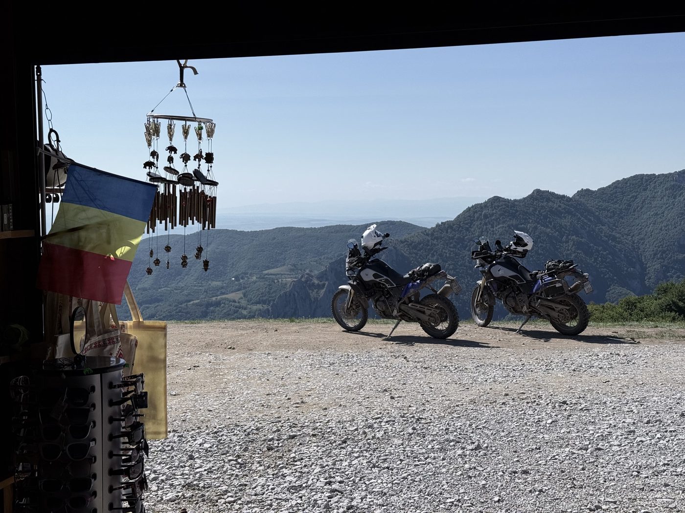 View from inside a roadside souvenir stall with a Romanian flag, motorcycles parked outside