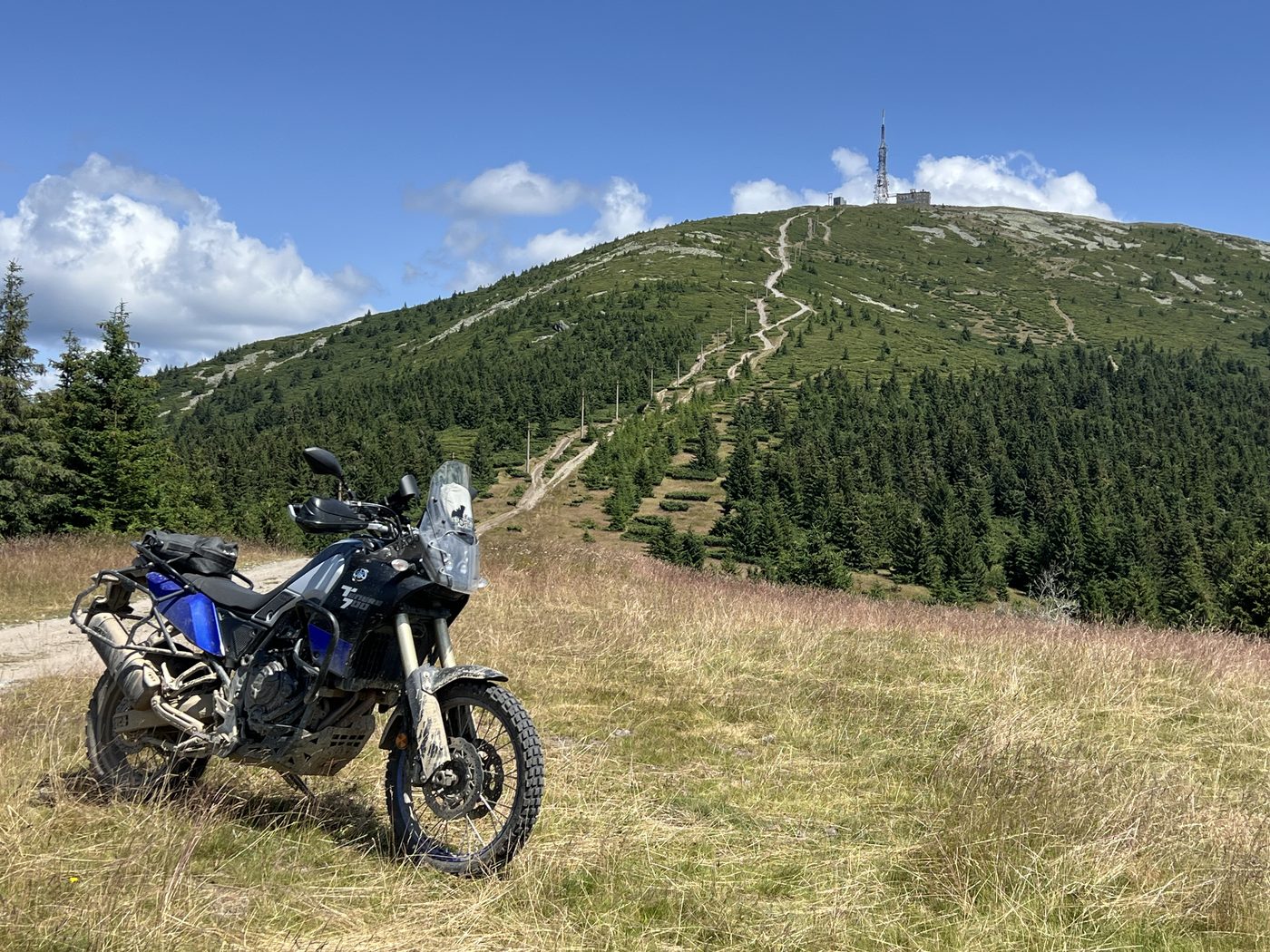 A motorcycle on a grass track below a summit with a transmitter mast